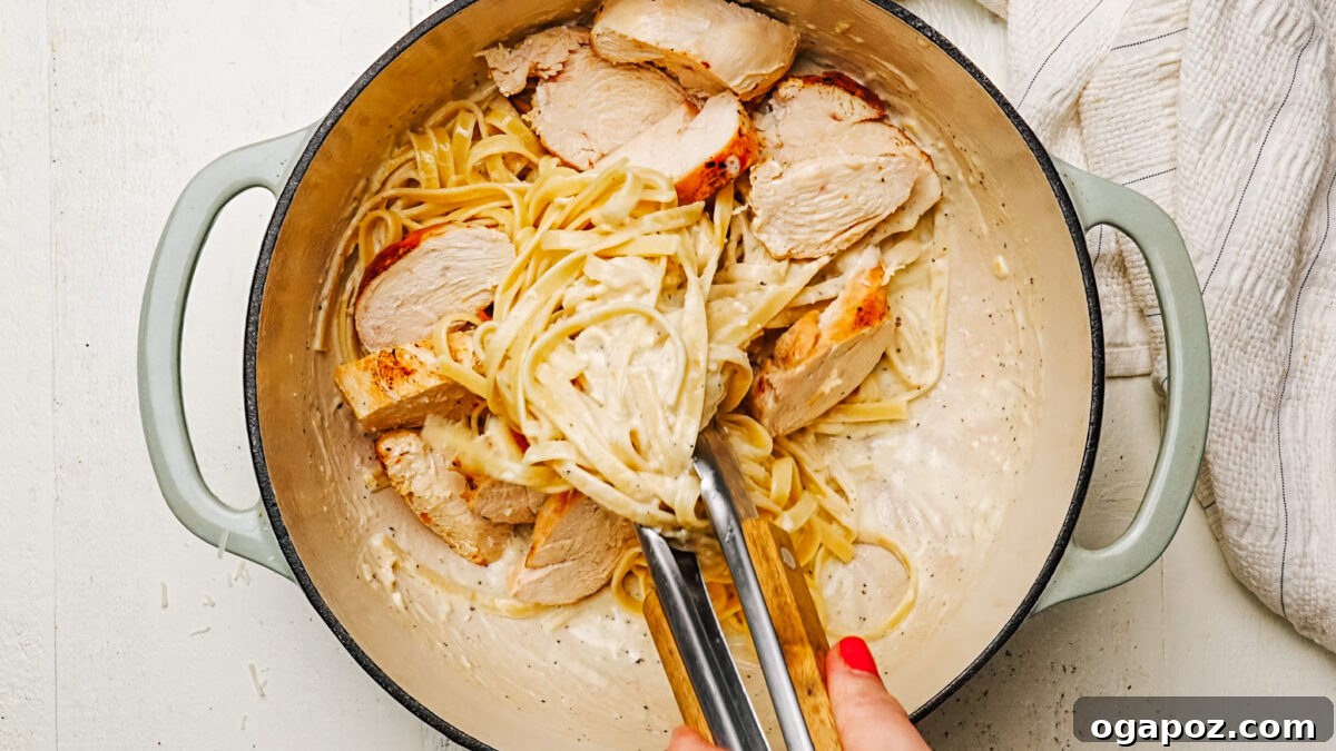 Rich and Creamy Chicken Alfredo 7 Combining sliced chicken and creamy Alfredo fettuccine in a large pan before serving.