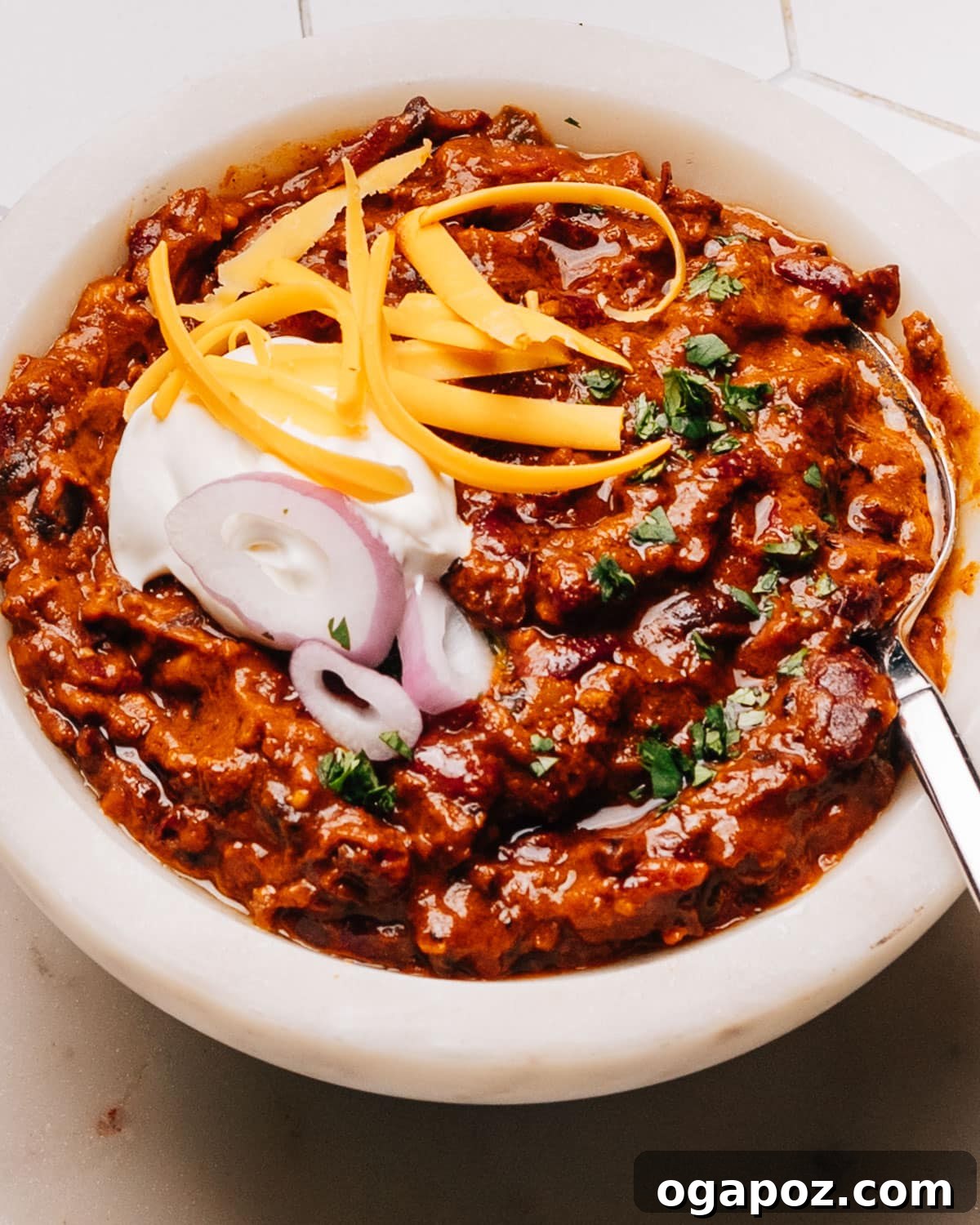 Finished Turkey Chili Crockpot Recipe in a bowl with a spoon, sour cream, onions and cheese, showcasing its rich texture and appealing presentation.