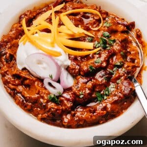 Finished Turkey Chili Crockpot Recipe in a bowl with a spoon, sour cream, onions and cheese.