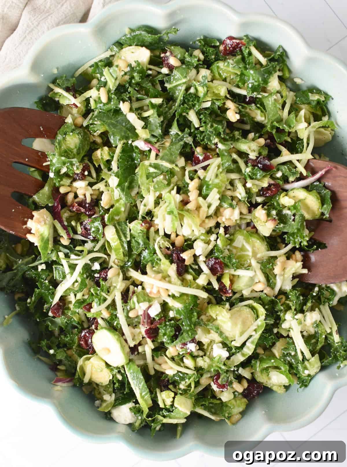 Shaved Brussels and Kale Salad 2 A large bowl of Kale Brussels Sprout Salad garnished with feta, cranberries, and pine nuts, with wooden serving spoons resting in the bowl.