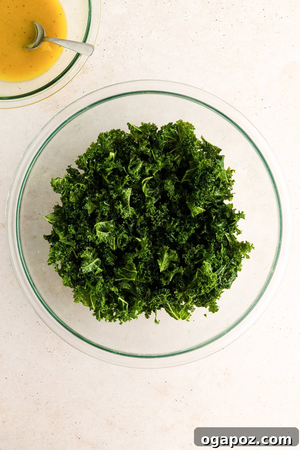 Chopped kale being massaged with dressing in a large mixing bowl.