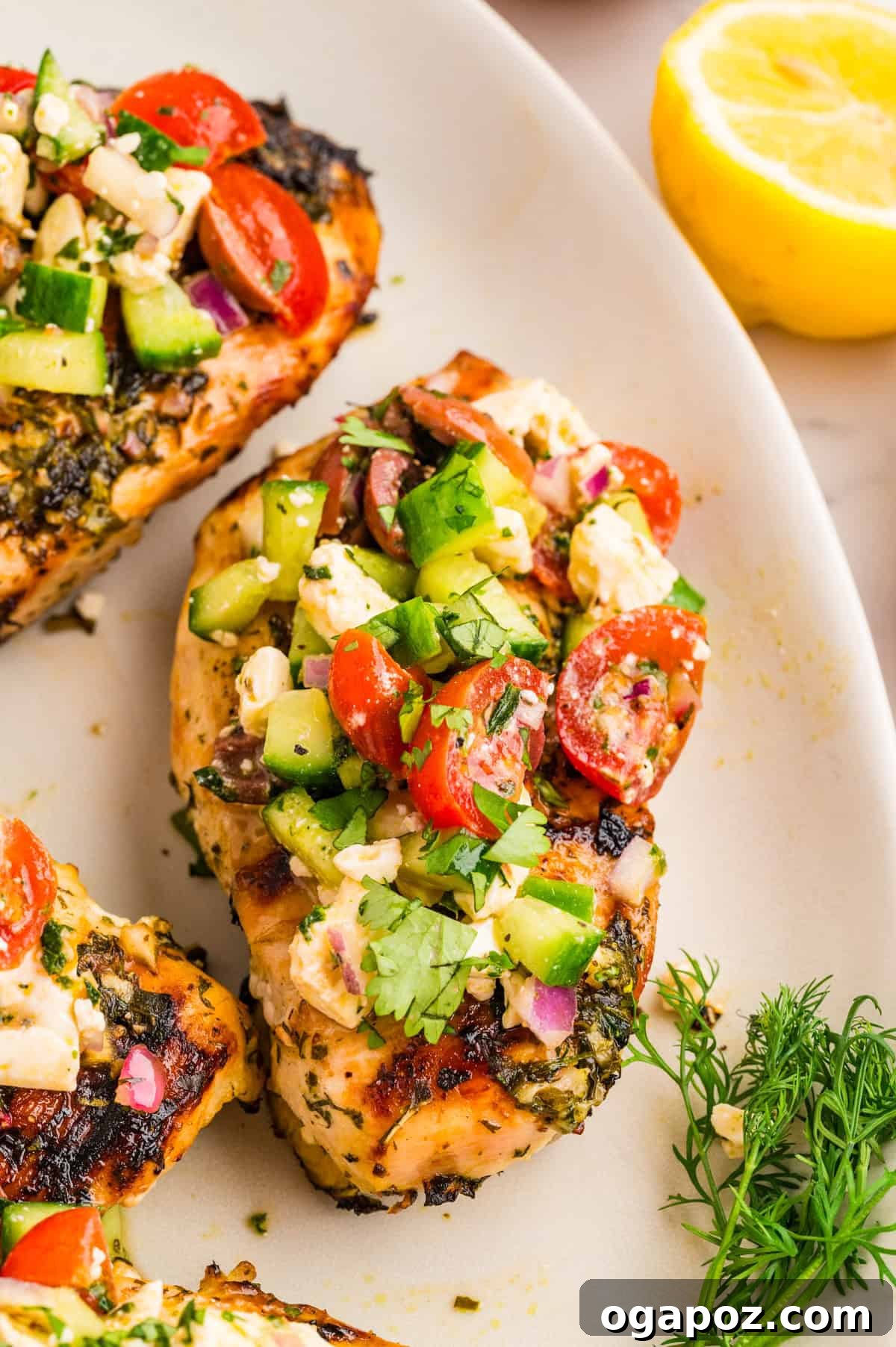Juicy Grilled Mediterranean chicken breast topped with a colorful cucumber, tomato, olive, and feta salad, served on a pristine white plate.