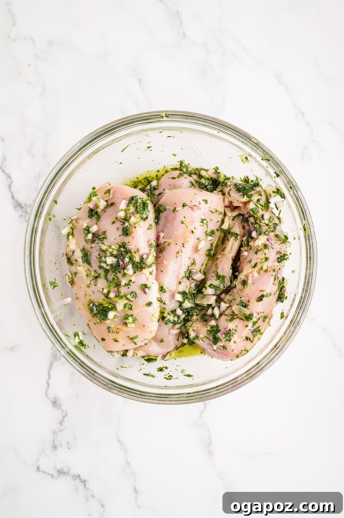 Chicken breasts marinating in a glass bowl, fully coated in the herb-lemon-olive oil marinade.