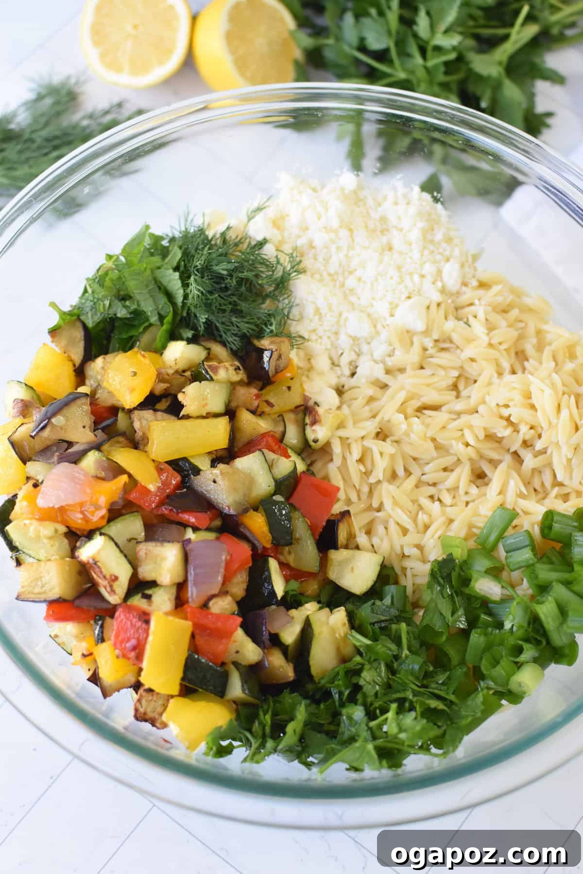 Mediterranean Roasted Vegetable Orzo Salad with Feta 8 Roasted vegetables mixed with cooked orzo pasta in a glass bowl, before adding dressing and herbs