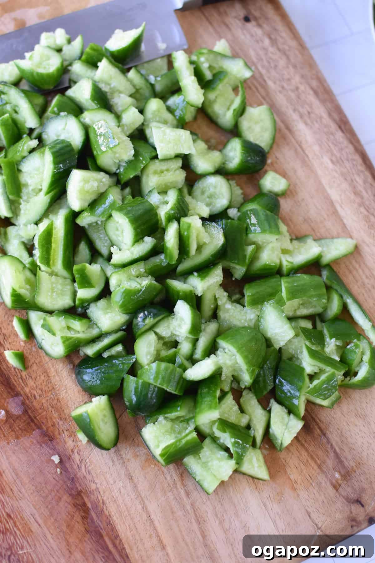 Hands smashing cucumbers with a cleaver on a cutting board, preparing them for the salad.