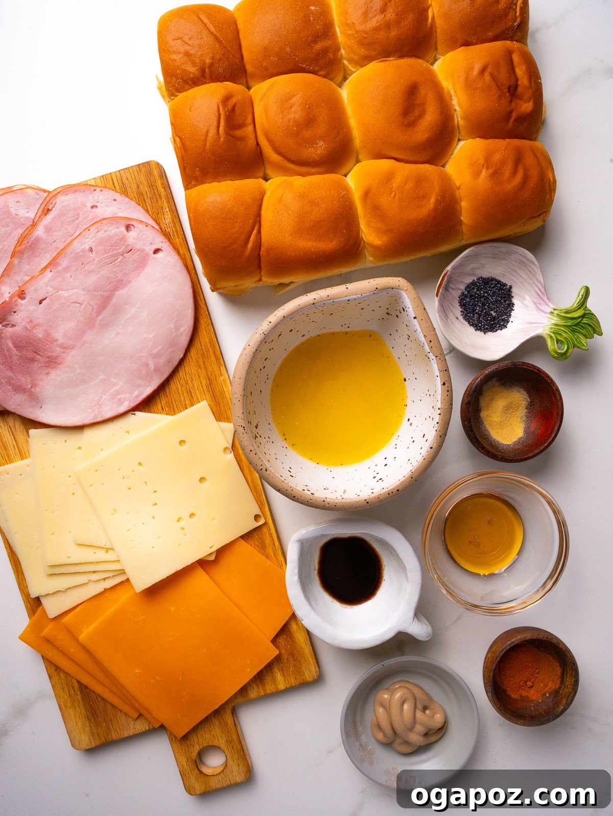 Buttery Honey-Glazed Ham & Cheese Sliders Recipe 3 Overhead view of ingredients for Hawaiian ham and cheese sliders: sweet Hawaiian rolls, deli ham, Swiss and cheddar, butter, Dijon, Worcestershire and poppy seeds.