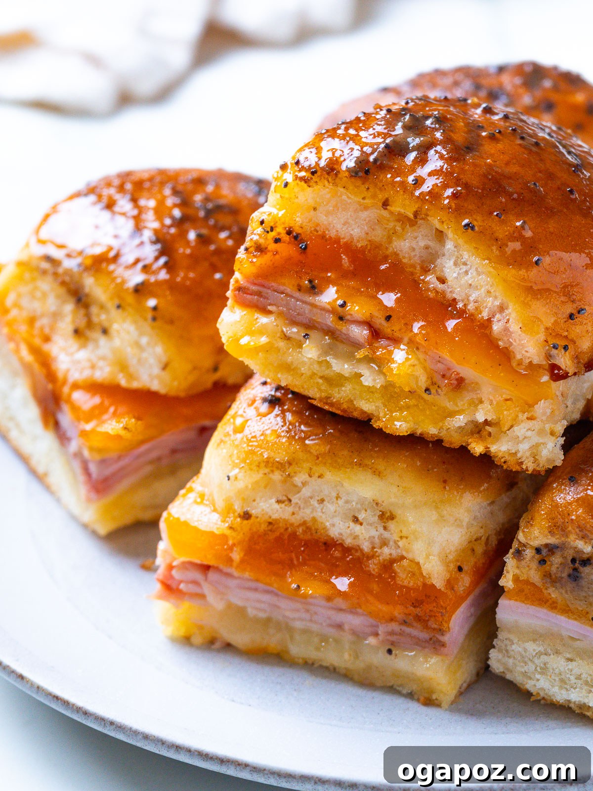 Buttery Honey-Glazed Ham & Cheese Sliders Recipe 8 A plate of stacked Hawaiian ham and cheese sliders with a glossy, poppy-seed-flecked glaze.