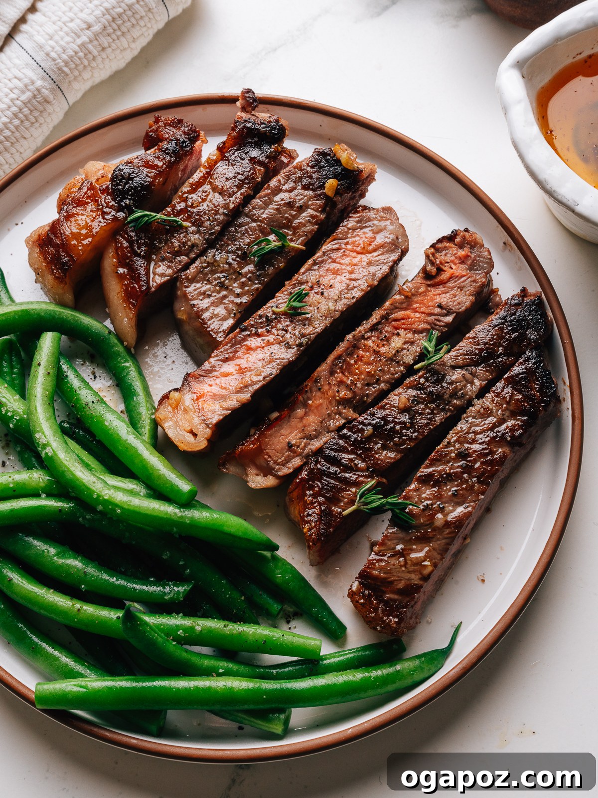 Pan-Seared Garlic Butter Steak Ready in 15 Minutes 8 Sliced garlic butter steak on a plate with green beans and a dish of garlic butter.