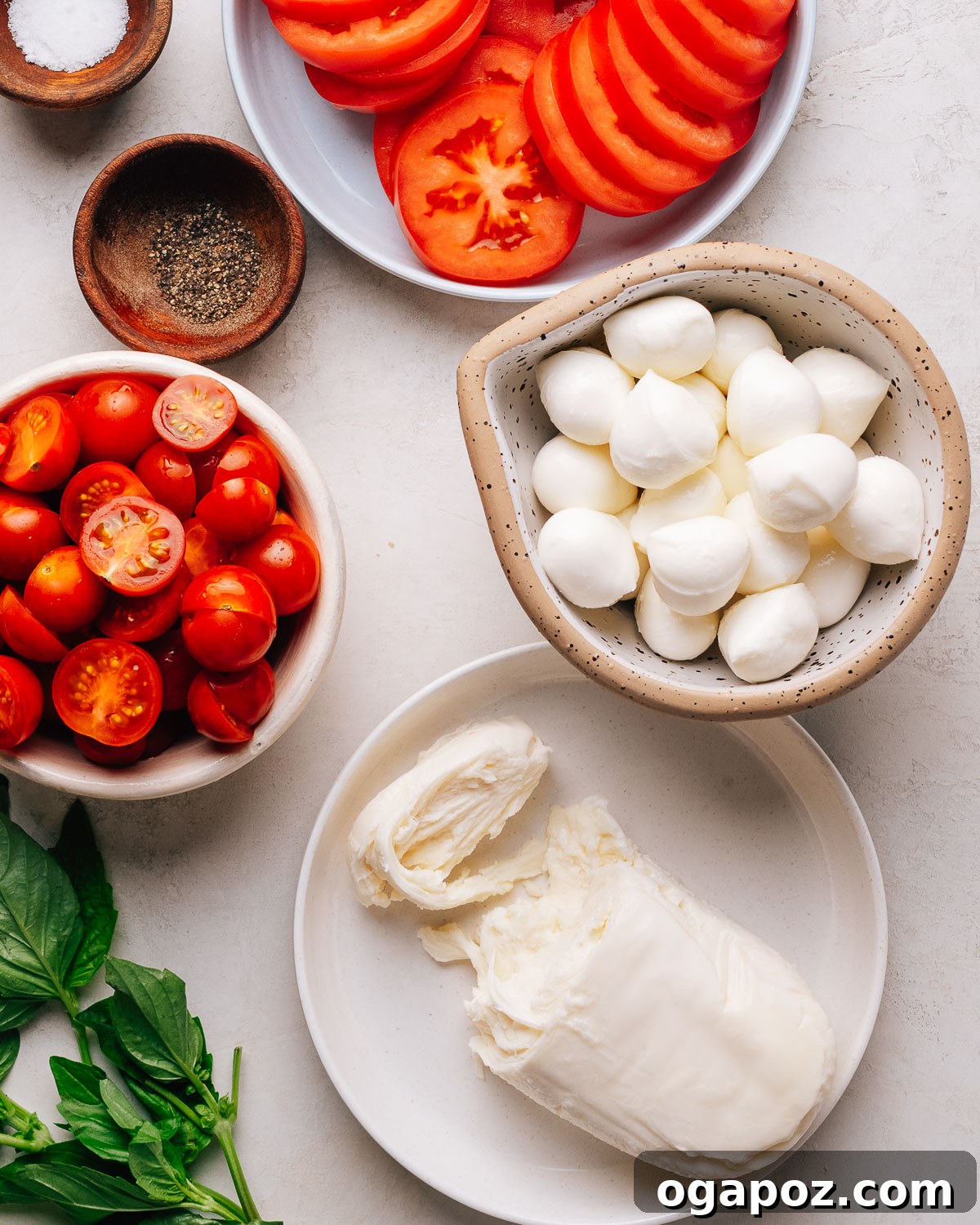 Authentic Caprese Salad with Cherry Tomatoes 3 Caprese Salad recipe ingredients with cherry tomatoes, mozzarella and basil on a white surface.