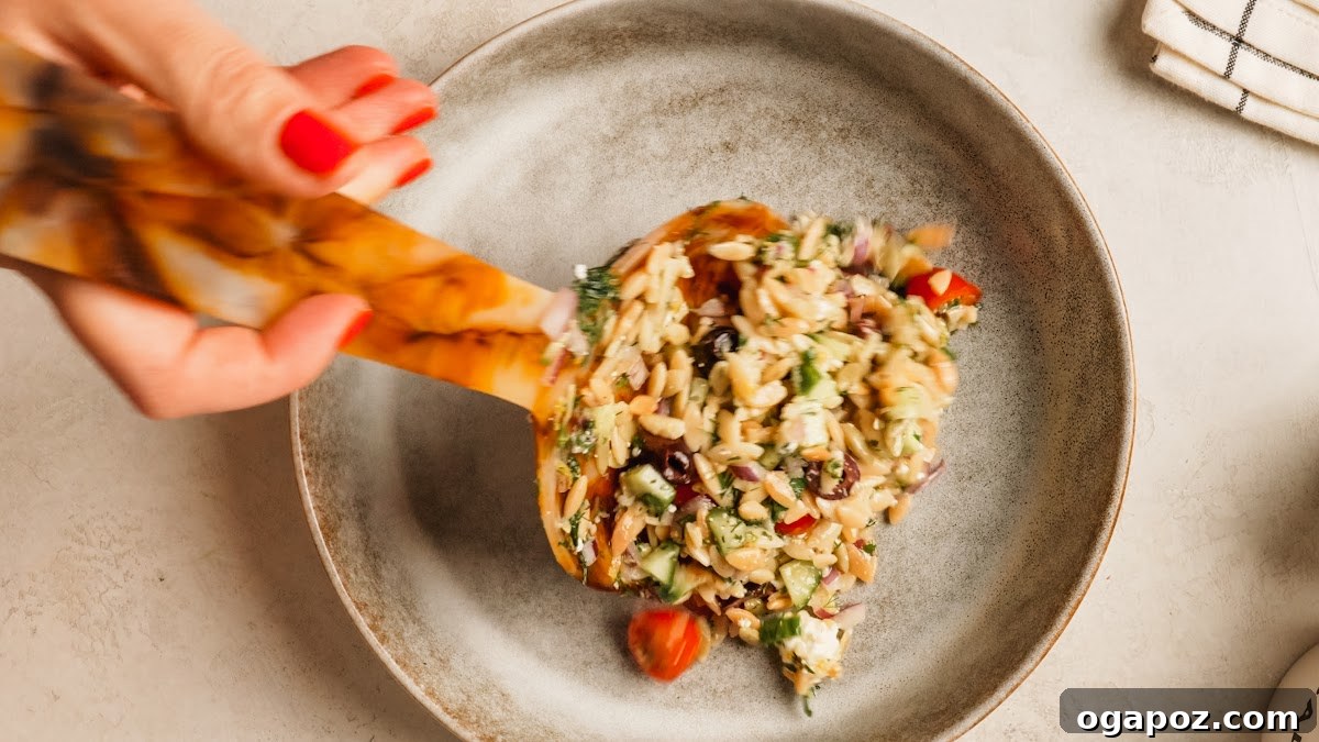 Mediterranean Orzo Salad with Feta, Olives & Cherry Tomatoes 9 A wooden spoon lifting a serving of orzo pasta salad from the bowl.