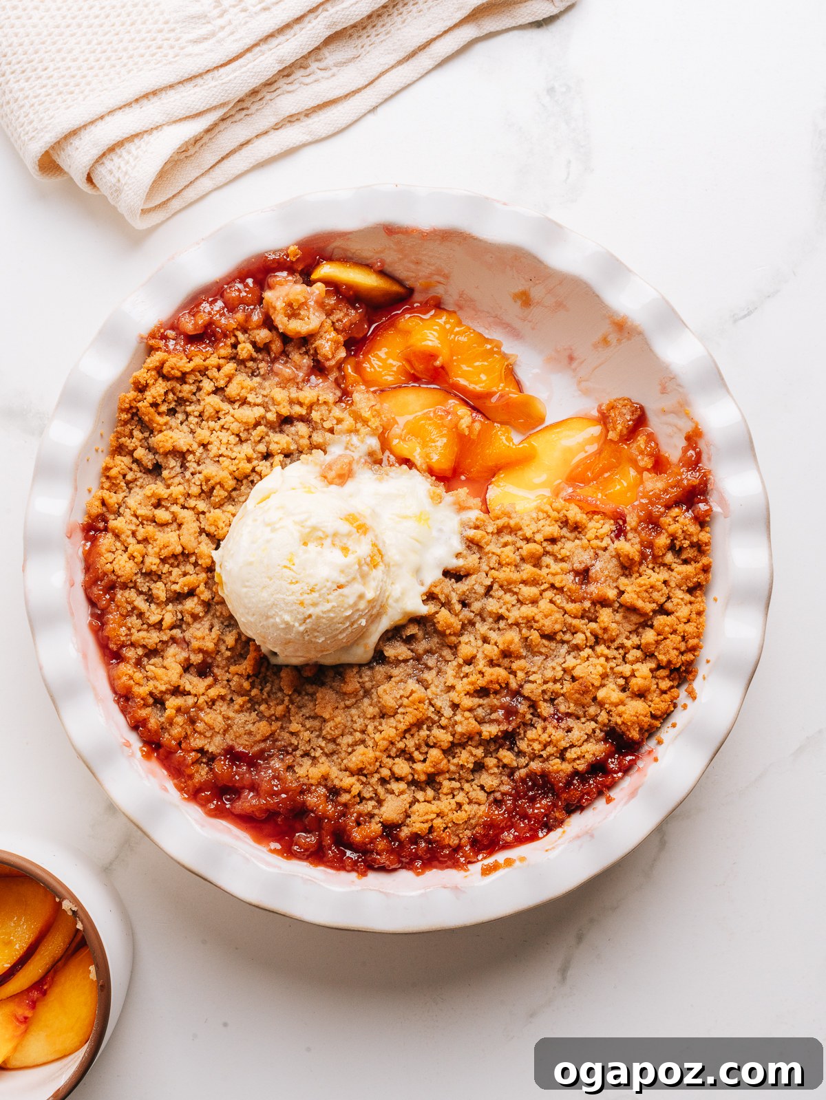 Juicy Peach Crumble with Crunchy Oat Topping 11 A pie dish of peach crumble with a scoop of vanilla ice cream.
