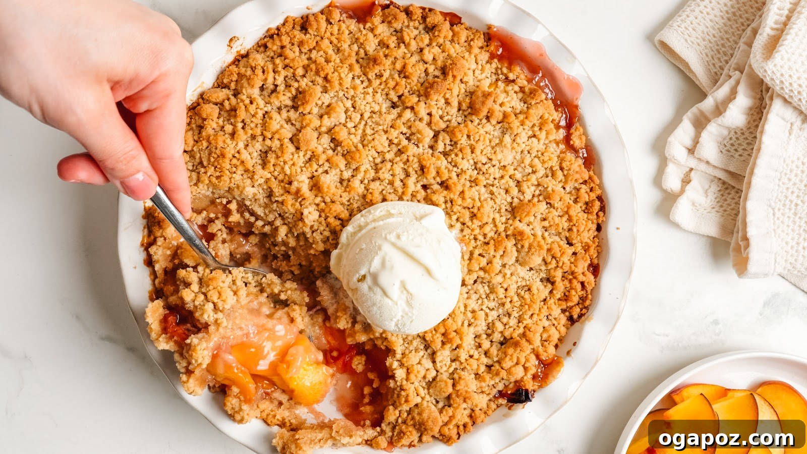 Juicy Peach Crumble with Crunchy Oat Topping 10 Baked peach crumble in a white pie dish with a scoop of vanilla ice cream melting on top.