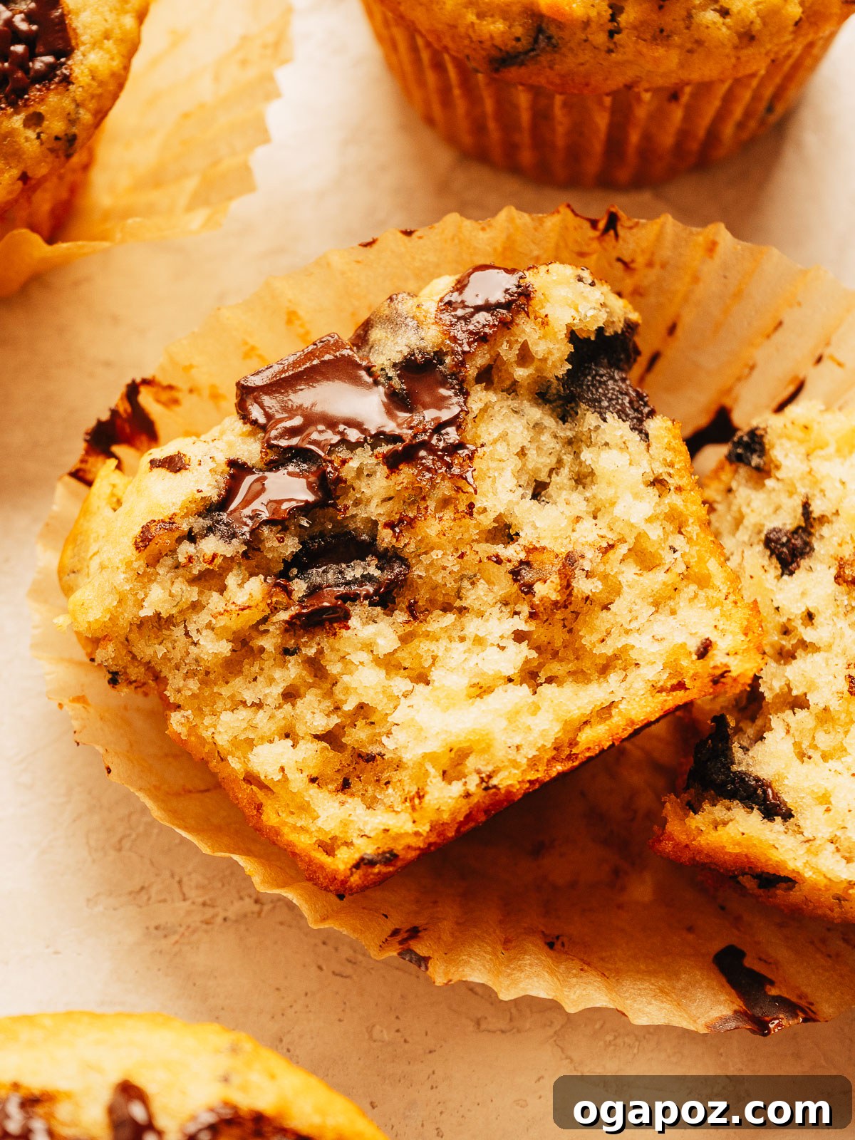 One-Bowl Banana Chocolate Chunk Muffins Soft and Moist 2 Banana chocolate chip muffins stacked on a plate with melty chocolate chunks on top.