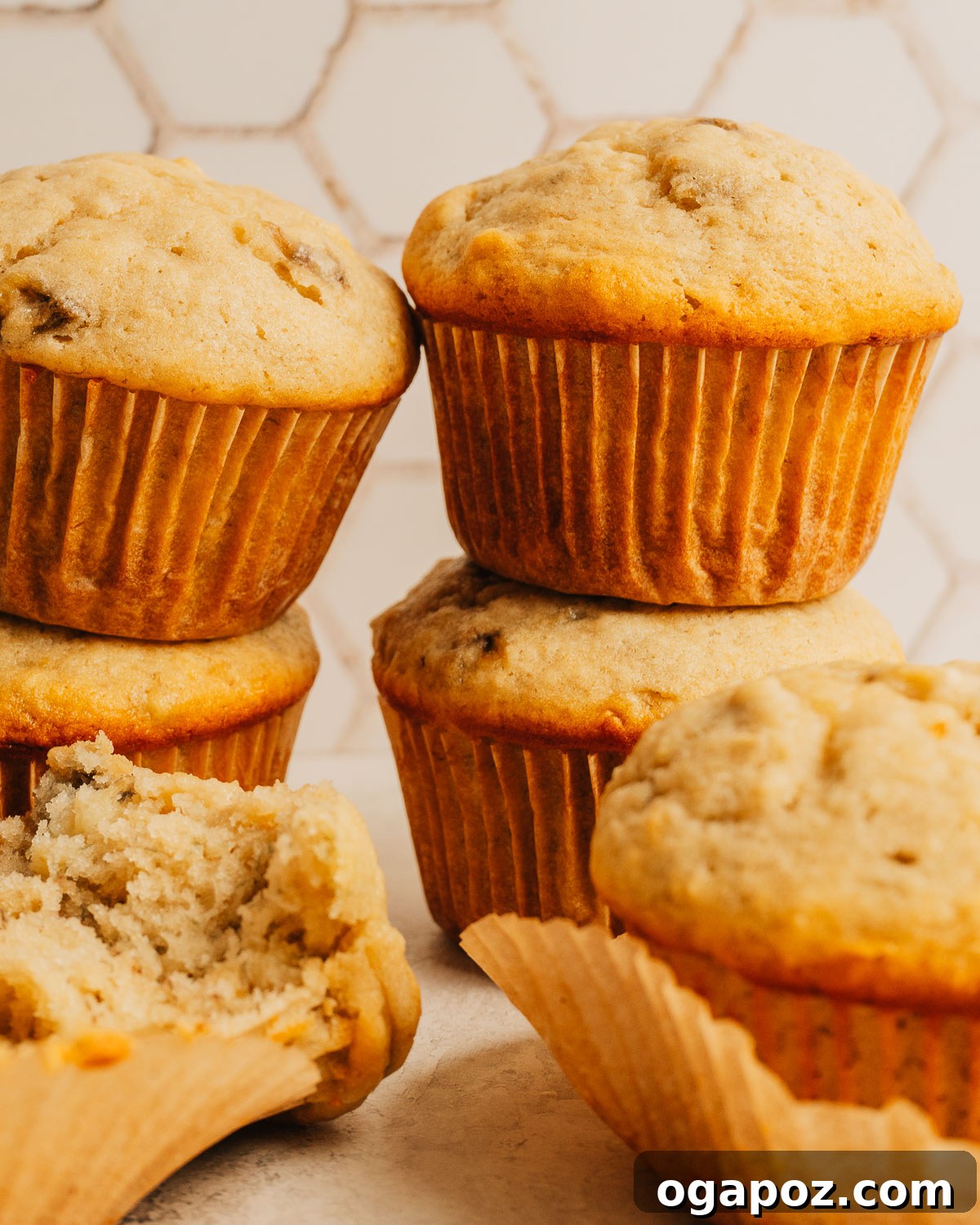 Moist Banana Bread Muffins That Stay Fresh for Days 2 A stack of golden banana bread muffins with tall domed tops on a white surface.