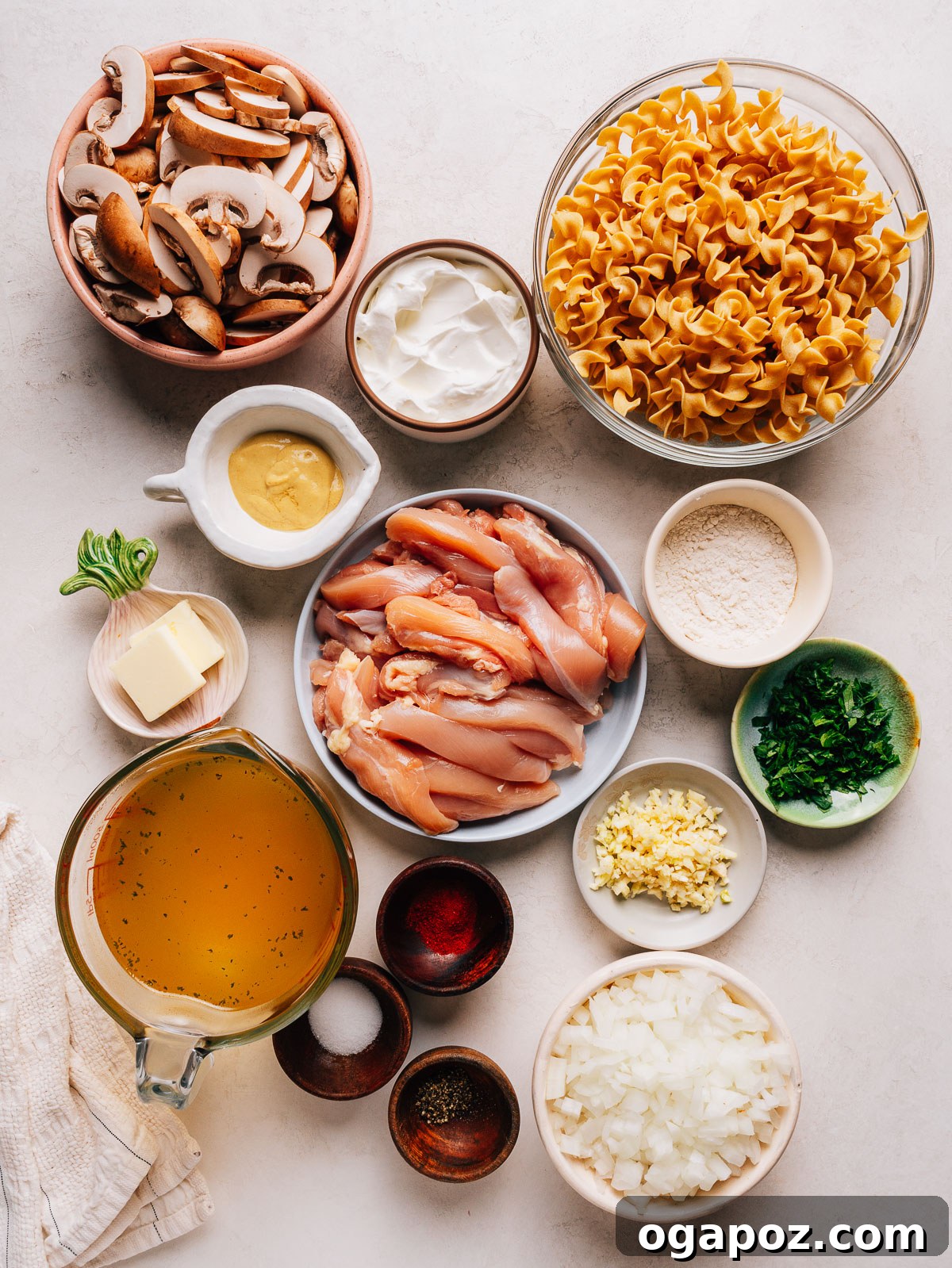Creamy One-Pan Chicken Stroganoff 3 Chicken stroganoff ingredients laid out in bowls, including chicken thighs, cremini mushrooms, egg noodles and sour cream.