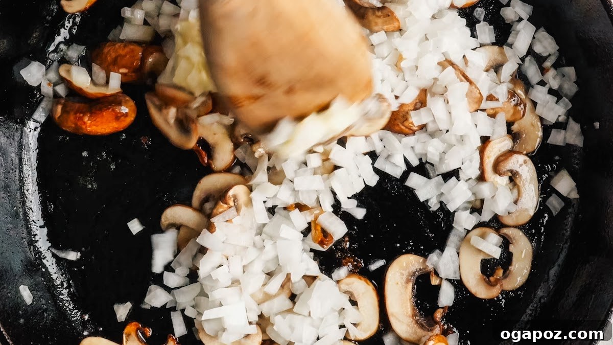 Creamy One-Pan Chicken Stroganoff 7 Adding sliced onion to the browned mushrooms in the skillet.