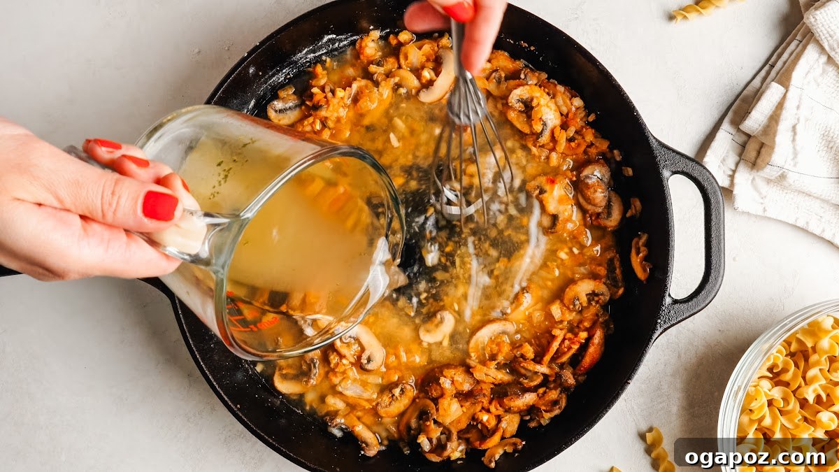 Creamy One-Pan Chicken Stroganoff 8 Whisking chicken broth into the skillet to build the sauce.