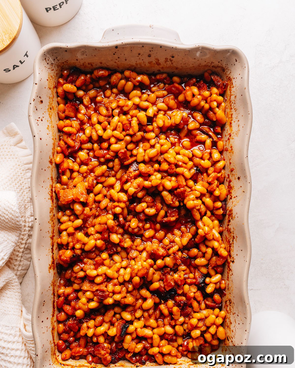 Overhead view of a baking dish of baked beans beside salt and pepper cellars.