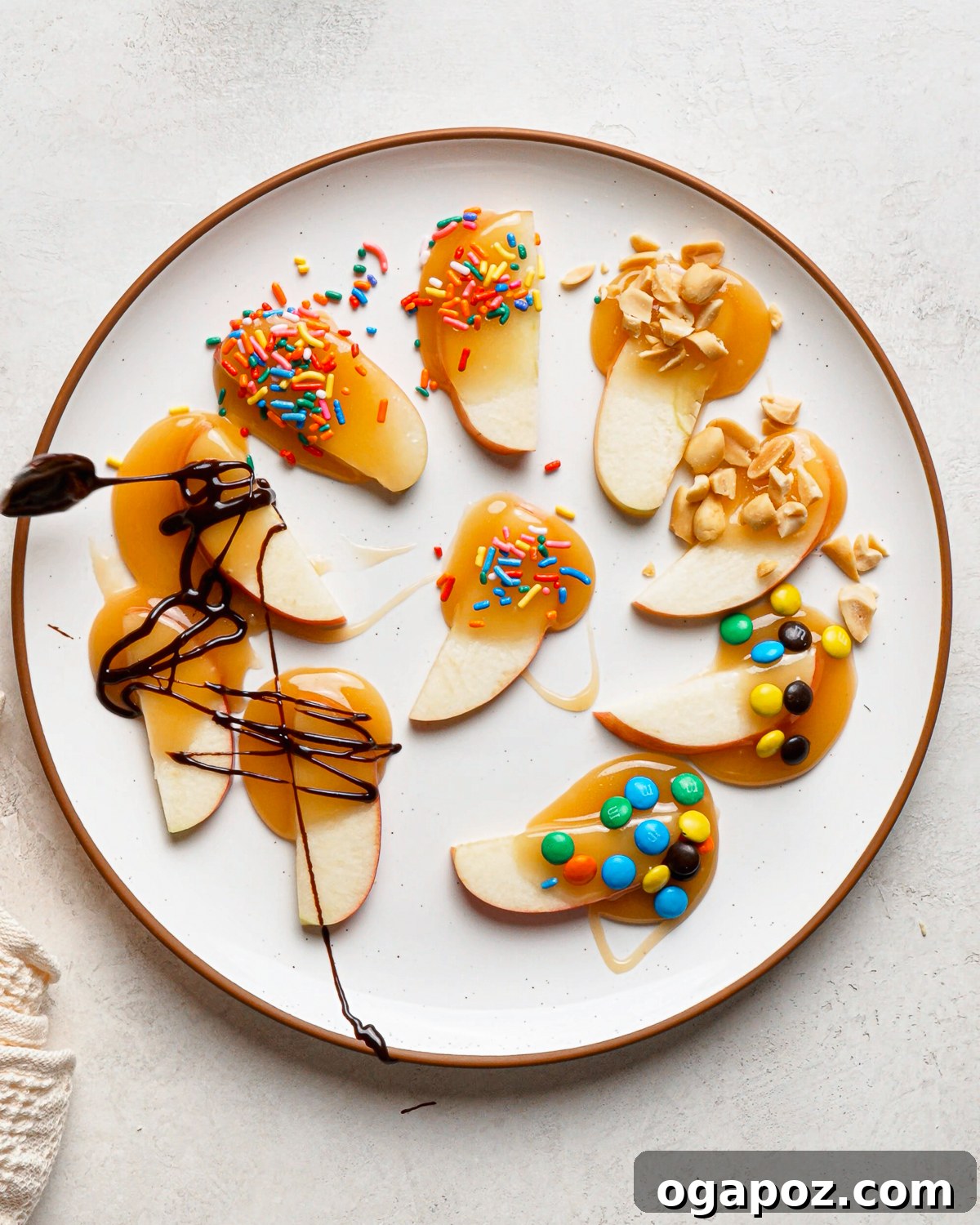 Plate of caramel apple slices topped with chocolate drizzle, sprinkles, M&M’s and chopped peanuts.