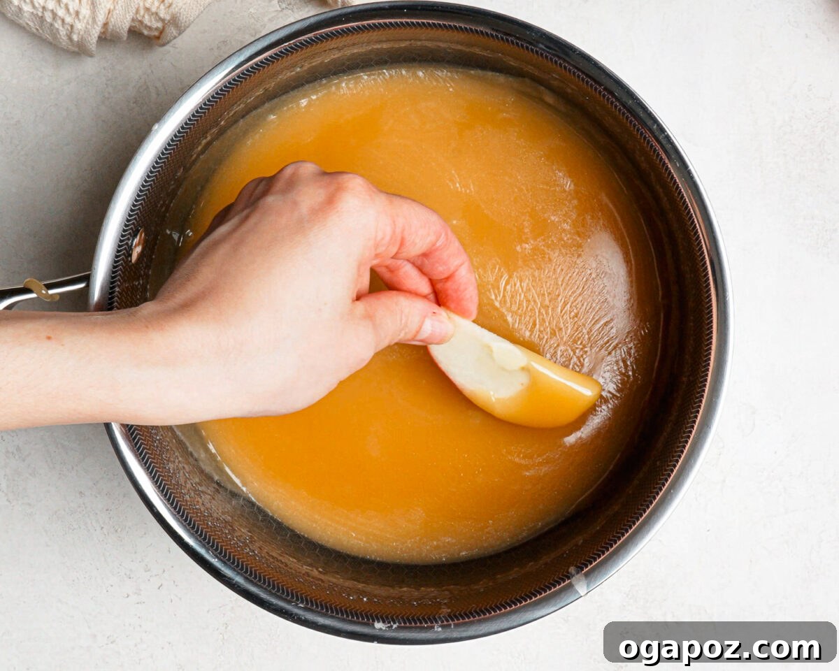 Dipping an apple slice into homemade caramel in a saucepan.