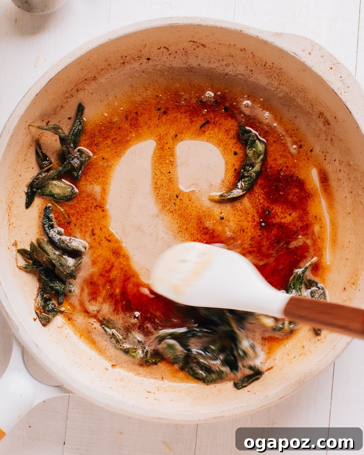 Finished brown butter sage sauce in a pan with a spatula and crisp sage leaves.