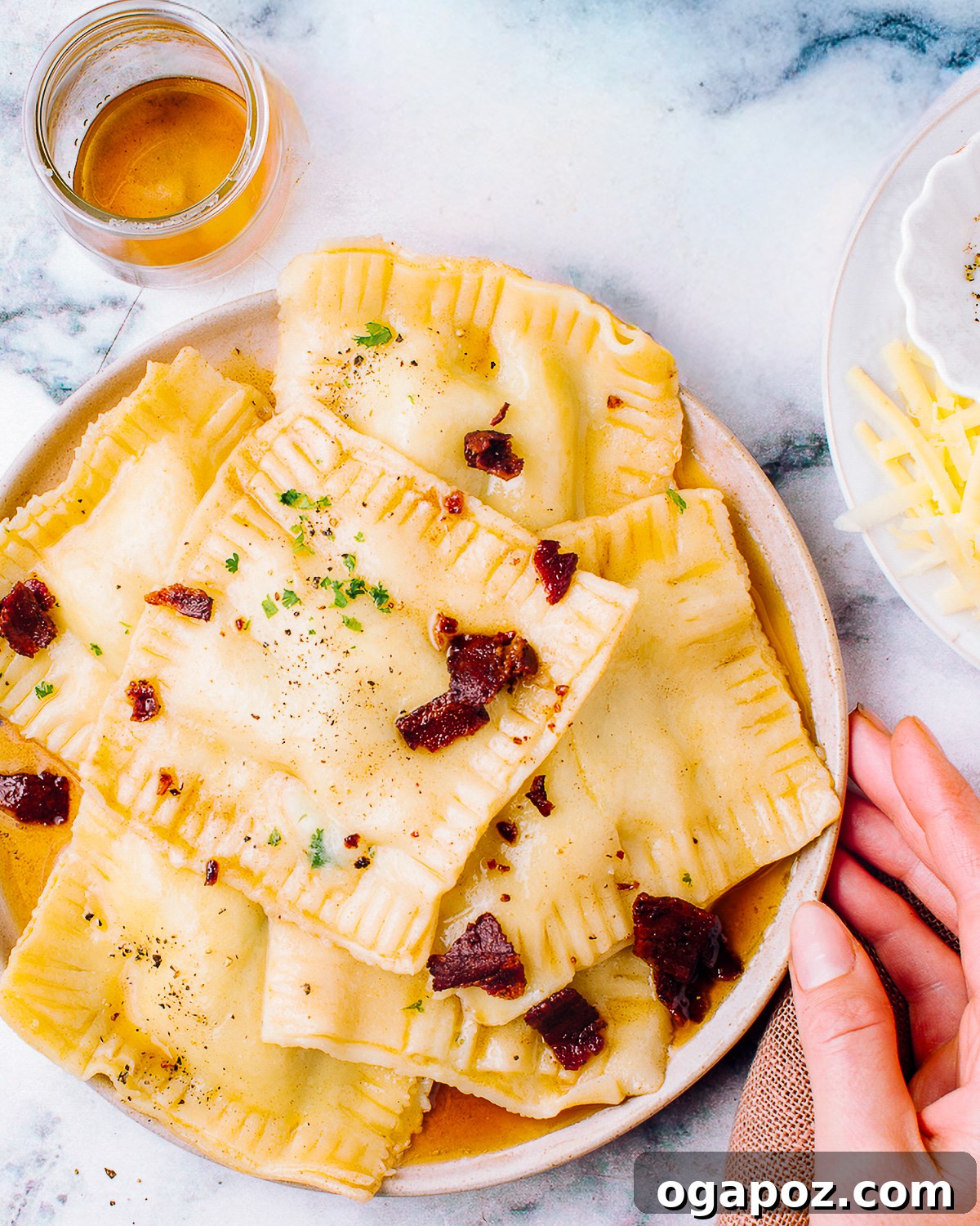 Overhead plate of butternut squash ravioli in brown butter sauce with grated parmesan alongside.