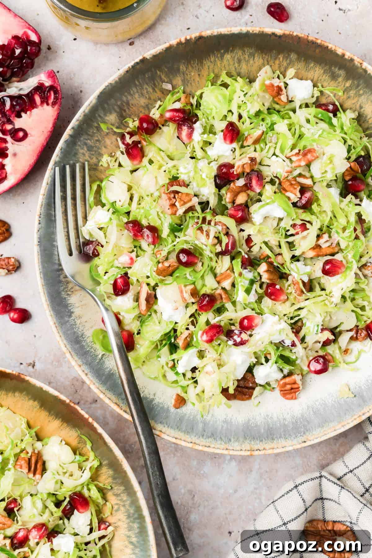 Shaved Brussels sprouts salad with pomegranate, pecans, and goat cheese on a table with scattered pomegranate arils